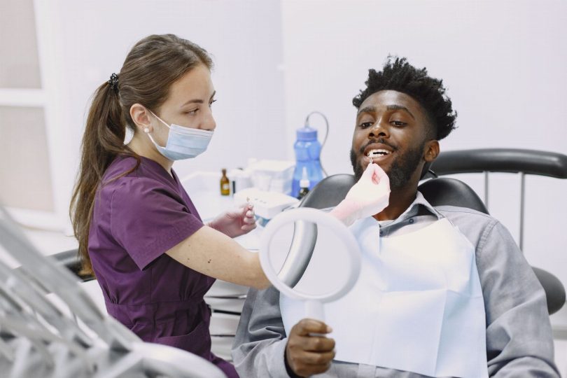 Dentista mostrando ao paciente modelo de facetas dentais resina e porcelana durante consulta
