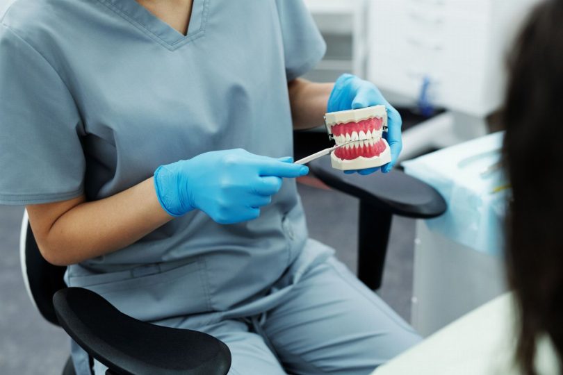 Dentista com modelo dentário e guia de cor avaliando lente de contato dental