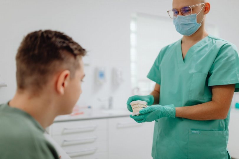 Dentista mostrando modelo de implante dentário para paciente em consultório